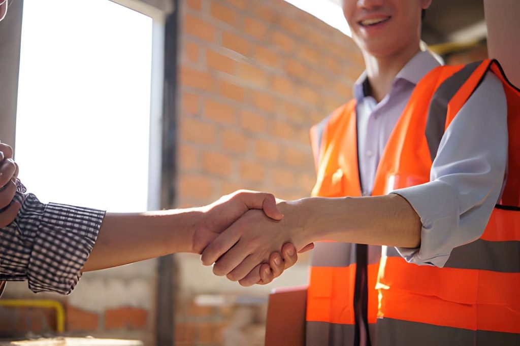 Home watch services Stuart FL professionals shaking hands at construction site with safety vest and brick wall background